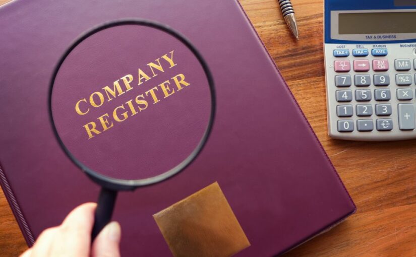 A book with the title Company Register seen through a magnifying glass and calculator next to the book.